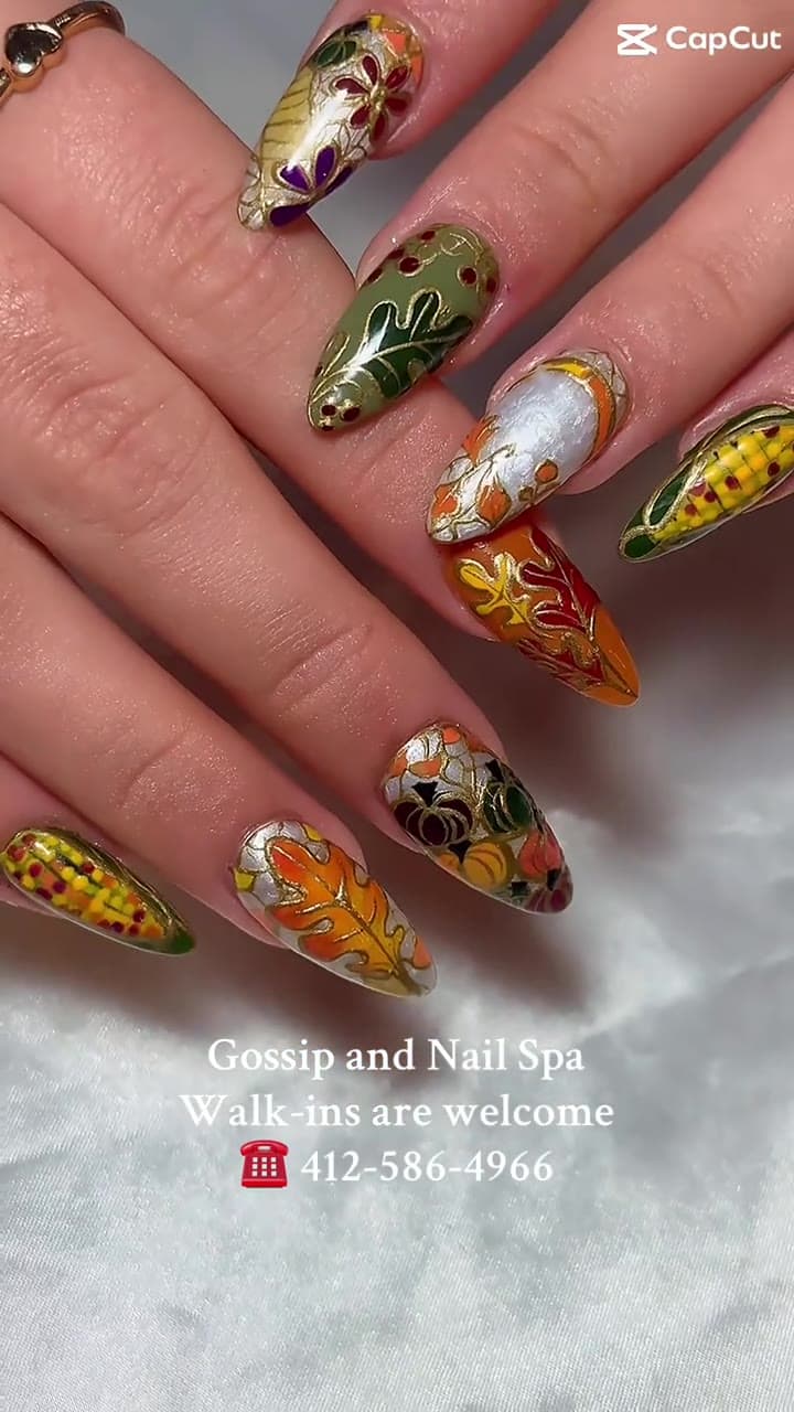 Thanksgiving harvest nail art — painted pumpkins, corn, and autumn leaves from TikTok @gossipandnailspa