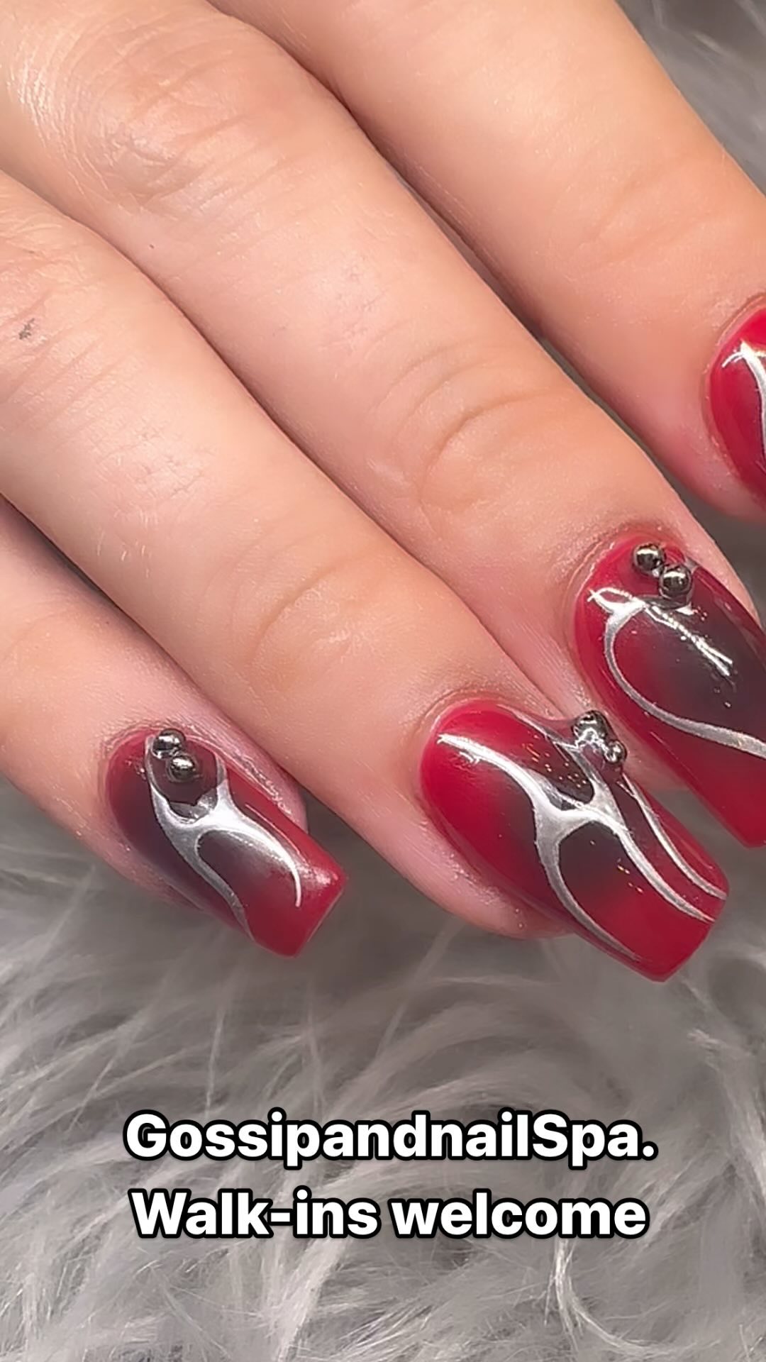 Dark red ombre nails with silver chrome swirls and studs